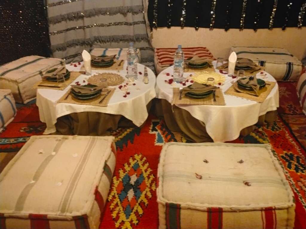 **"Romantic dinner setup in the Agafay Desert, Marrakech, featuring a beautifully decorated nomadic tent with lanterns, traditional Moroccan cushions, and a cozy dining arrangement under a starry night sky."**